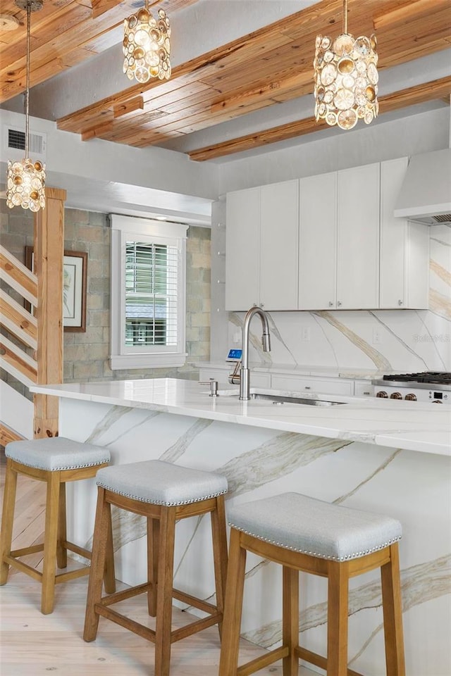 kitchen featuring beam ceiling, a chandelier, decorative backsplash, wood ceiling, and wall chimney range hood