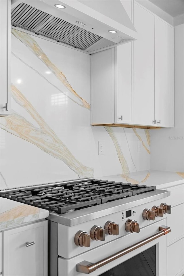 kitchen view of stove, custom range hood, white cabinetry, and light stone countertops