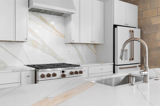 kitchen with wall chimney range hood, stove, white cabinets, and light stone countertops