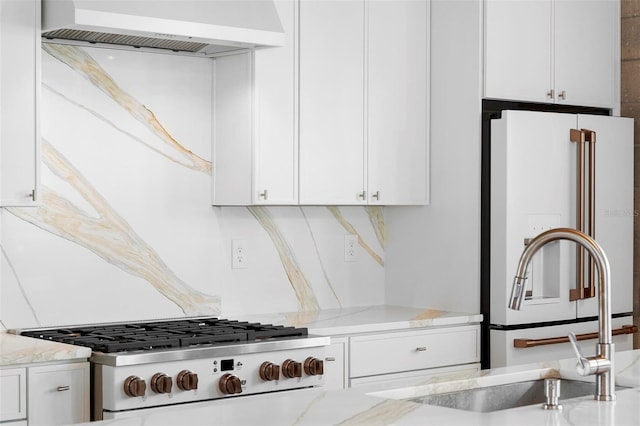 kitchen with wall chimney range hood, freestanding refrigerator, stove, white cabinets, and light stone counters