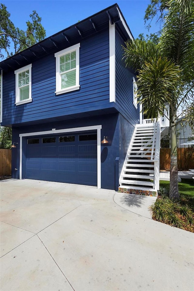 view of front facade with a garage, stairs, driveway, fence, and stucco siding