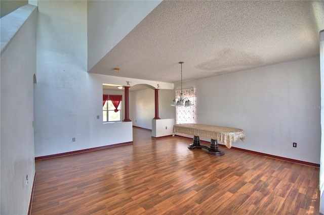 unfurnished dining area featuring arched walkways, baseboards, wood finished floors, and a textured ceiling