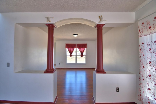 interior space with arched walkways, dark wood-style floors, a textured ceiling, and ornate columns