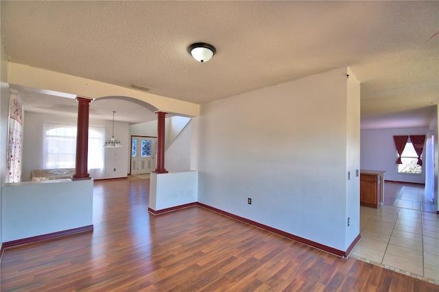 unfurnished room with visible vents, wood finished floors, a healthy amount of sunlight, and decorative columns