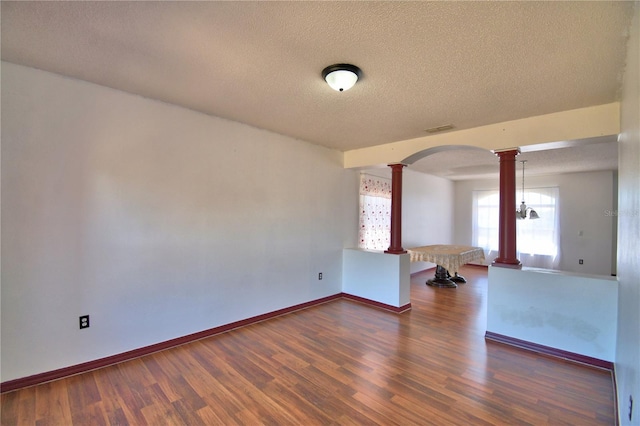 empty room featuring a textured ceiling, arched walkways, dark wood-style flooring, visible vents, and ornate columns