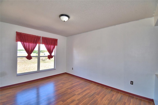 unfurnished room featuring baseboards, wood finished floors, and a textured ceiling