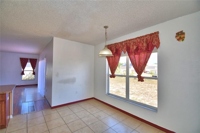 unfurnished dining area with baseboards, a textured ceiling, and light tile patterned floors