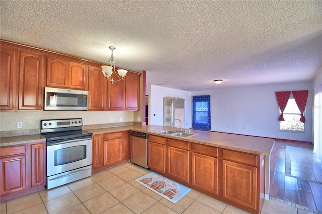 kitchen with light tile patterned floors, a sink, a peninsula, appliances with stainless steel finishes, and a notable chandelier