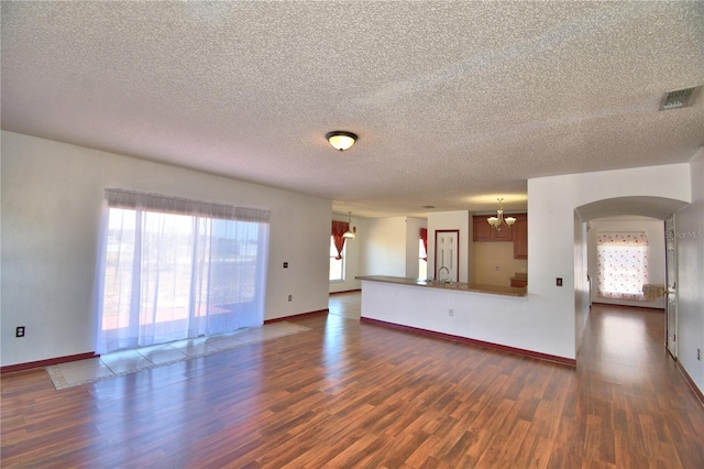 unfurnished living room featuring visible vents, an inviting chandelier, a textured ceiling, and dark wood finished floors