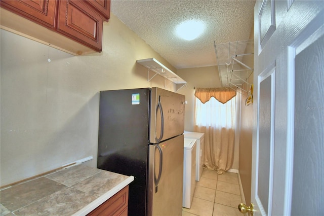kitchen featuring a textured ceiling, light tile patterned flooring, freestanding refrigerator, tile counters, and washer / dryer