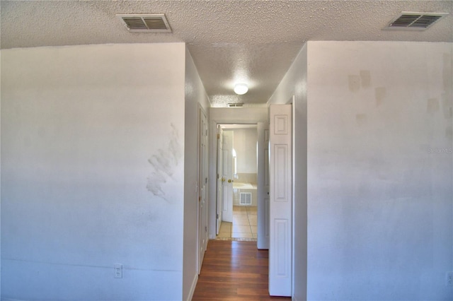 hallway featuring wood finished floors, visible vents, and a textured ceiling
