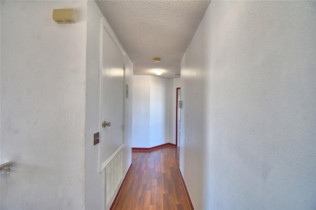 hall featuring a textured ceiling, visible vents, baseboards, and dark wood-style flooring