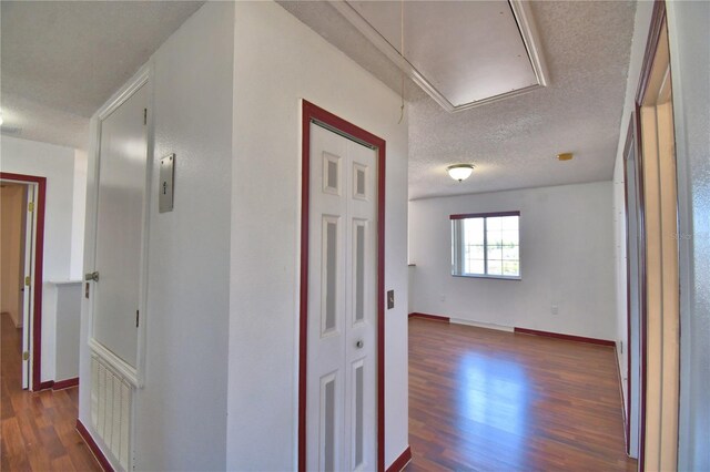 hallway featuring attic access, baseboards, a textured ceiling, and dark wood finished floors