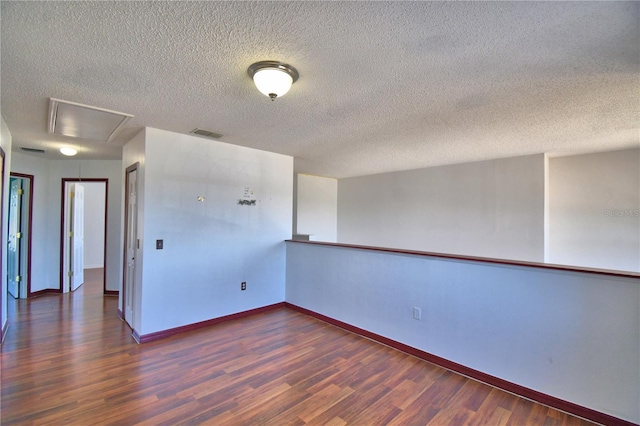 empty room with attic access, wood finished floors, visible vents, and baseboards
