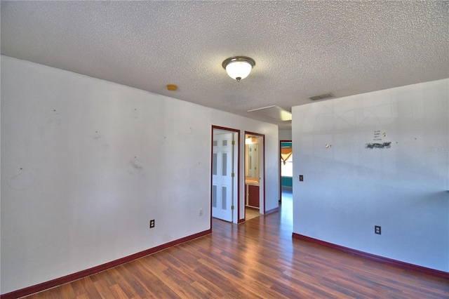 spare room with a textured ceiling, wood finished floors, visible vents, and baseboards
