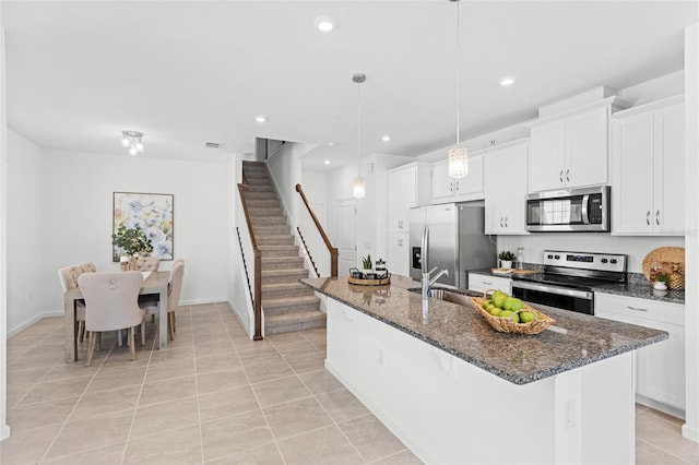 kitchen featuring an island with sink, light tile patterned floors, white cabinets, stainless steel appliances, and a sink