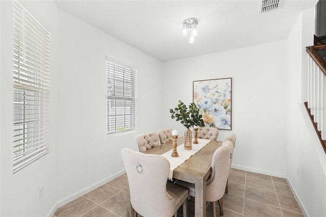 dining room with light tile patterned floors, baseboards, visible vents, and stairway