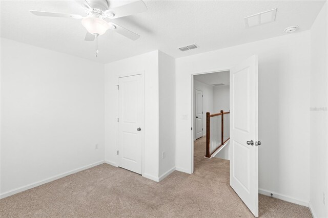 unfurnished bedroom featuring visible vents, light colored carpet, baseboards, and ceiling fan