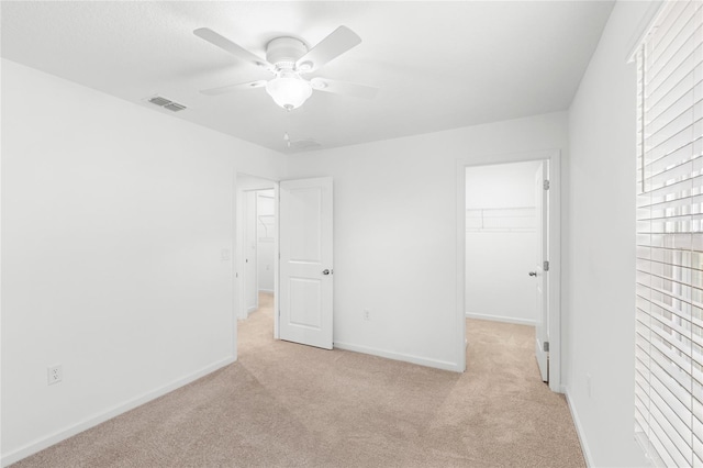unfurnished bedroom featuring light carpet, a walk in closet, visible vents, and a closet