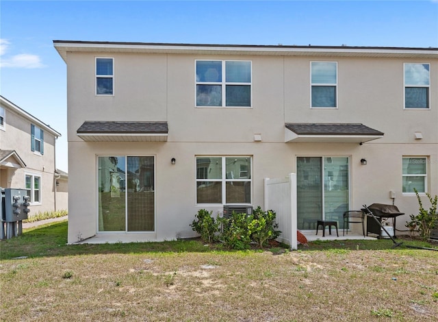 back of property with a lawn, stucco siding, and a shingled roof