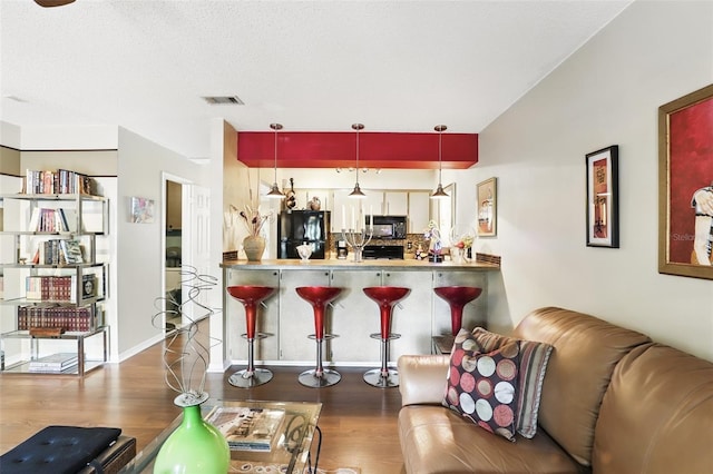 kitchen featuring visible vents, black appliances, a breakfast bar, wood finished floors, and decorative light fixtures