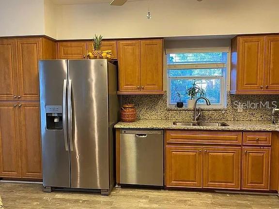 19430 SW 100th Loop, Dunnellon, FL 34432 - kitchen with stainless steel appliances, a sink, light stone counters, decorative backsplash, and light wood-type flooring