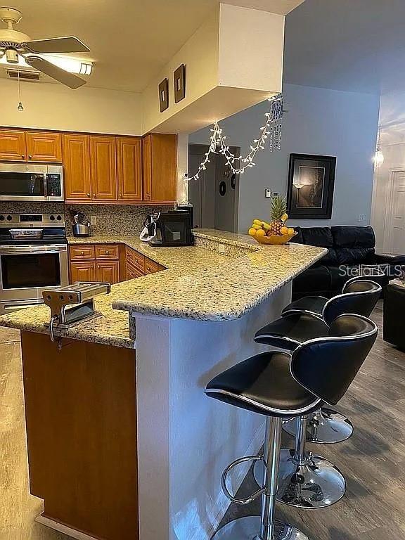 19430 SW 100th Loop, Dunnellon, FL 34432 - kitchen featuring appliances with stainless steel finishes, brown cabinets, a peninsula, light stone countertops, and a breakfast bar