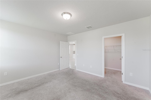 unfurnished bedroom featuring visible vents, a closet, a spacious closet, a textured ceiling, and carpet floors