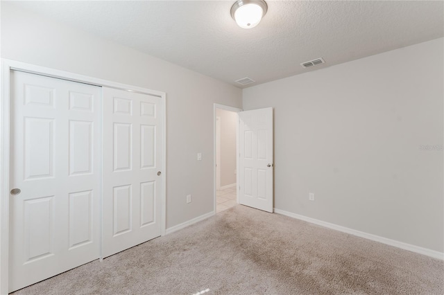 unfurnished bedroom with visible vents, baseboards, a closet, a textured ceiling, and carpet flooring