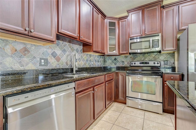 kitchen featuring reddish brown cabinets, a sink, dark stone counters, decorative backsplash, and appliances with stainless steel finishes