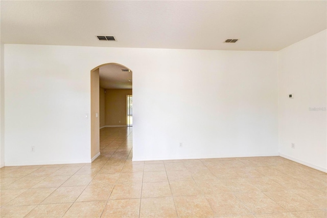 spare room featuring baseboards, arched walkways, visible vents, and light tile patterned floors