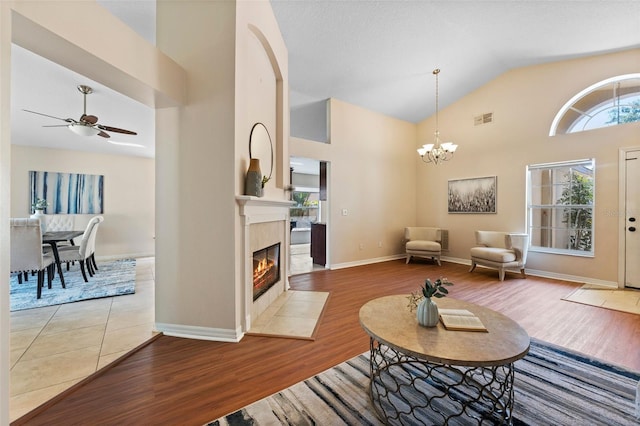 living room with high vaulted ceiling, wood finished floors, visible vents, and ceiling fan with notable chandelier