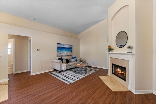 living room featuring wood finished floors, a tile fireplace, lofted ceiling, and baseboards