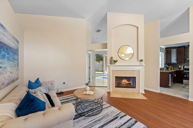 living room featuring high vaulted ceiling, light wood-style floors, visible vents, and a fireplace
