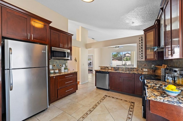 kitchen featuring dark stone counters, vaulted ceiling, a sink, decorative backsplash, and stainless steel appliances