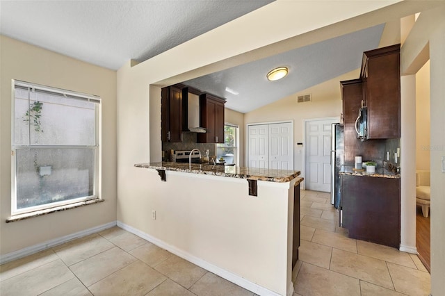 kitchen featuring stainless steel appliances, a kitchen breakfast bar, dark brown cabinets, stone countertops, and wall chimney range hood