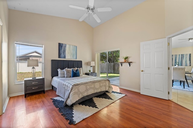 bedroom with baseboards, wood finished floors, high vaulted ceiling, and access to exterior