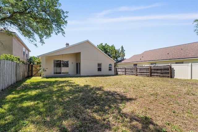 rear view of property featuring a fenced backyard, a yard, and stucco siding