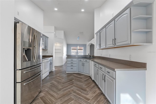 kitchen with dark countertops, a sink, white appliances, a peninsula, and recessed lighting