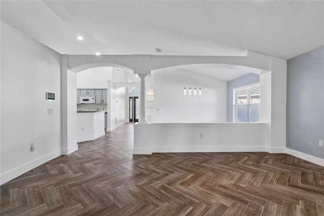 empty room with arched walkways, decorative columns, visible vents, baseboards, and recessed lighting