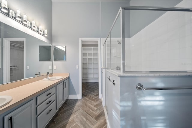 full bath with a sink, double vanity, tiled shower, baseboards, and a spacious closet