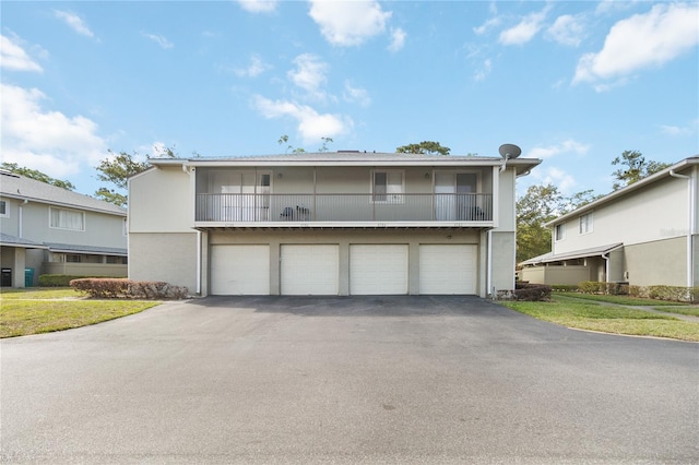 view of front of home featuring a front yard, a balcony, a garage, stucco siding, and driveway