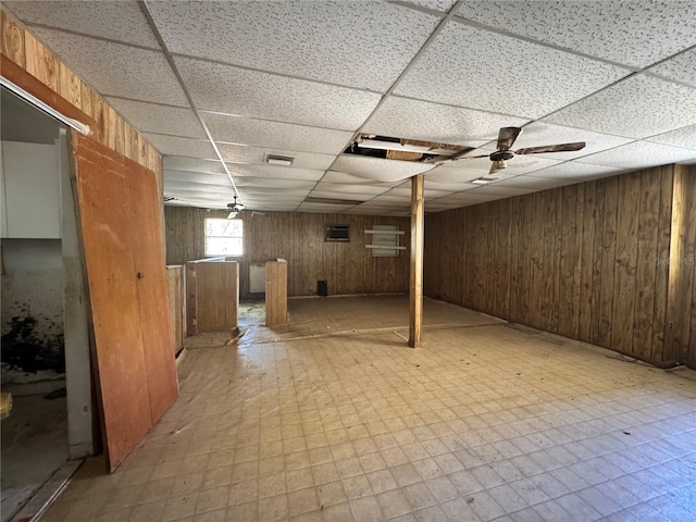 below grade area with wood walls, light floors, and a drop ceiling