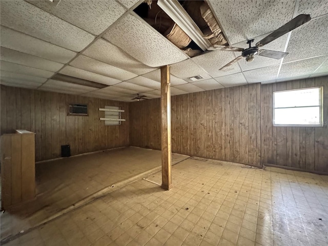 below grade area featuring visible vents, wooden walls, and a drop ceiling