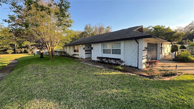 view of side of home with an attached garage, stucco siding, a lawn, and roof with shingles