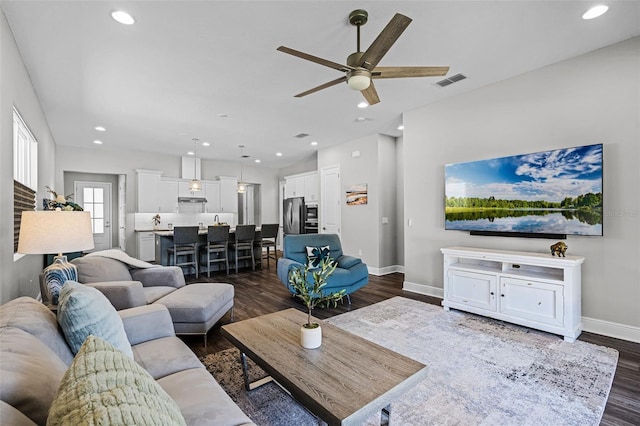 living area with dark wood finished floors, visible vents, a ceiling fan, and baseboards