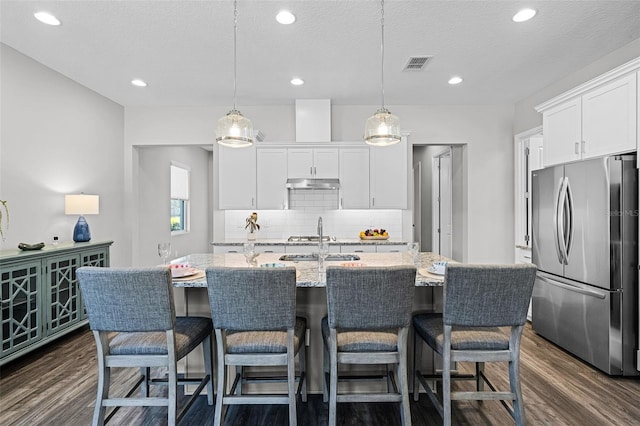 kitchen featuring dark wood-style flooring, under cabinet range hood, visible vents, and freestanding refrigerator