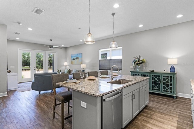 kitchen with stainless steel dishwasher, light stone counters, a sink, dark wood finished floors, and visible vents