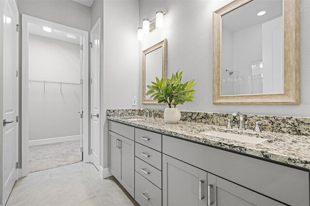full bath featuring a walk in closet, double vanity, tiled shower, and a sink