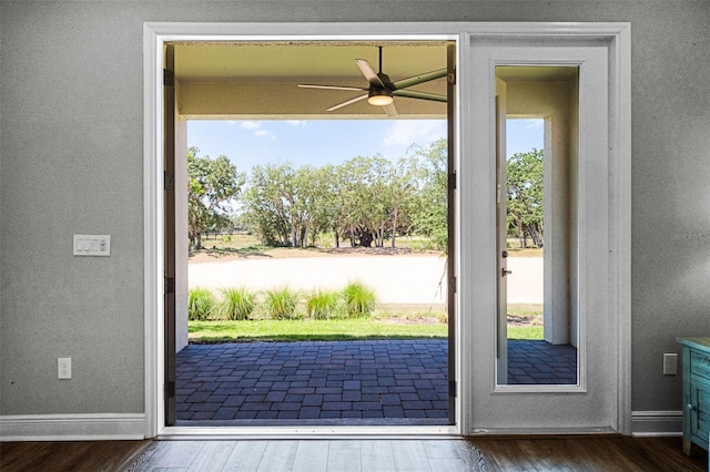doorway with a textured wall, baseboards, a ceiling fan, and wood finished floors